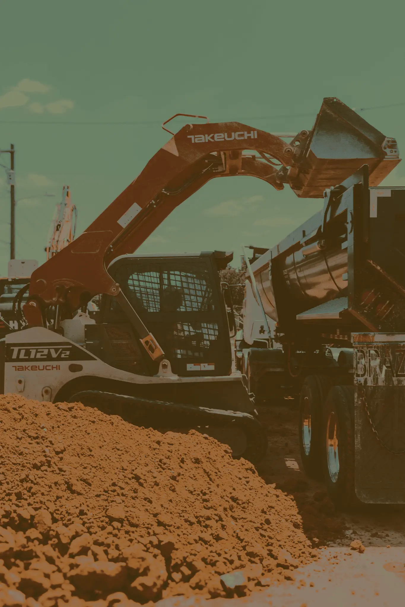 A skid-steer loading up an eighteen wheeler with dirt.